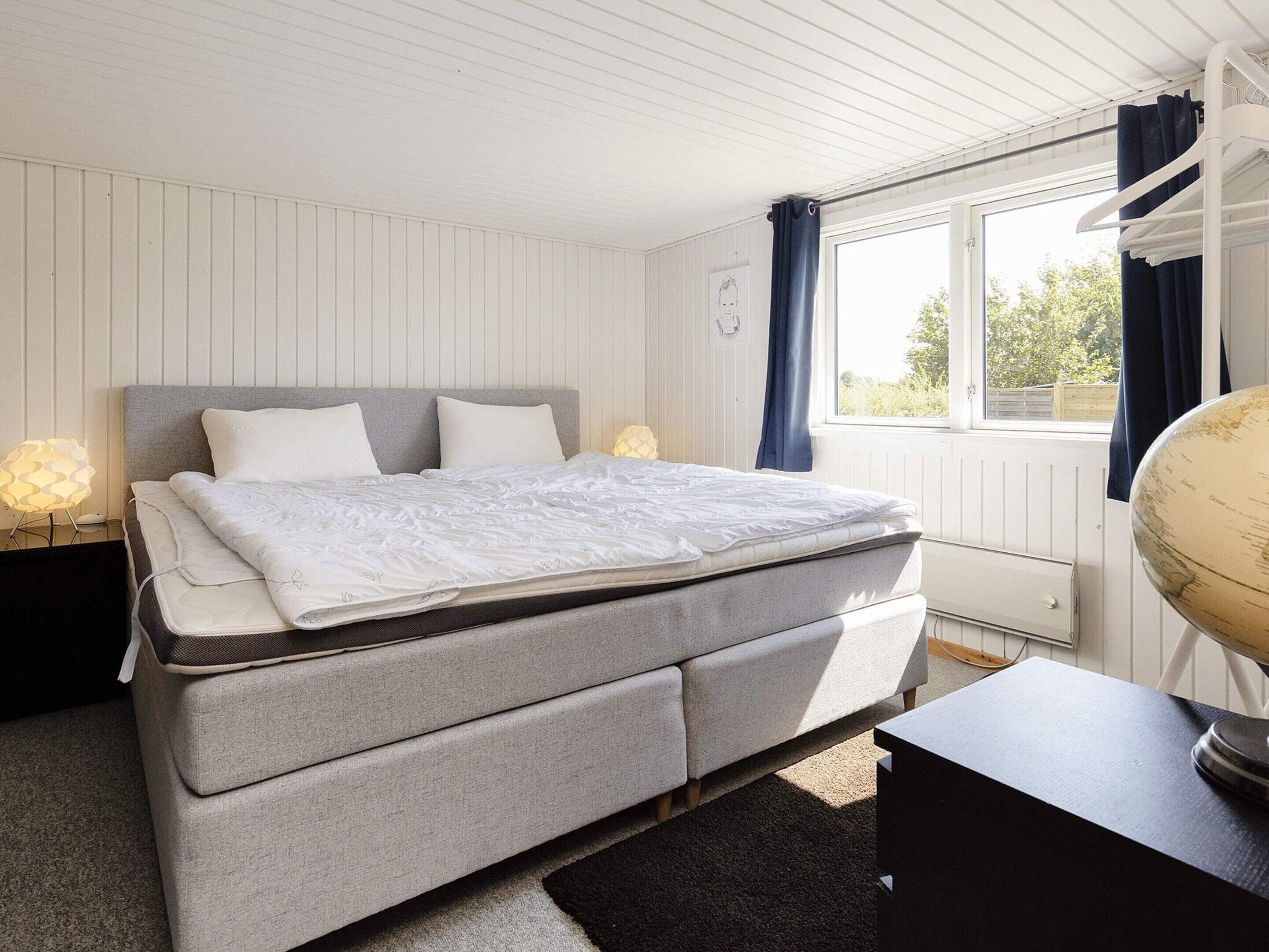 Quarto com cama, abajures, um globo em uma mesa e uma janela com cortinas.