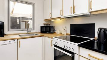 A compact kitchen with white cabinets, a black stove, a microwave, and a coffee maker.