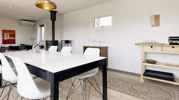 Uma área de refeições moderna com uma mesa branca, cadeiras pretas e uma luminária pendente preta e dourada.
