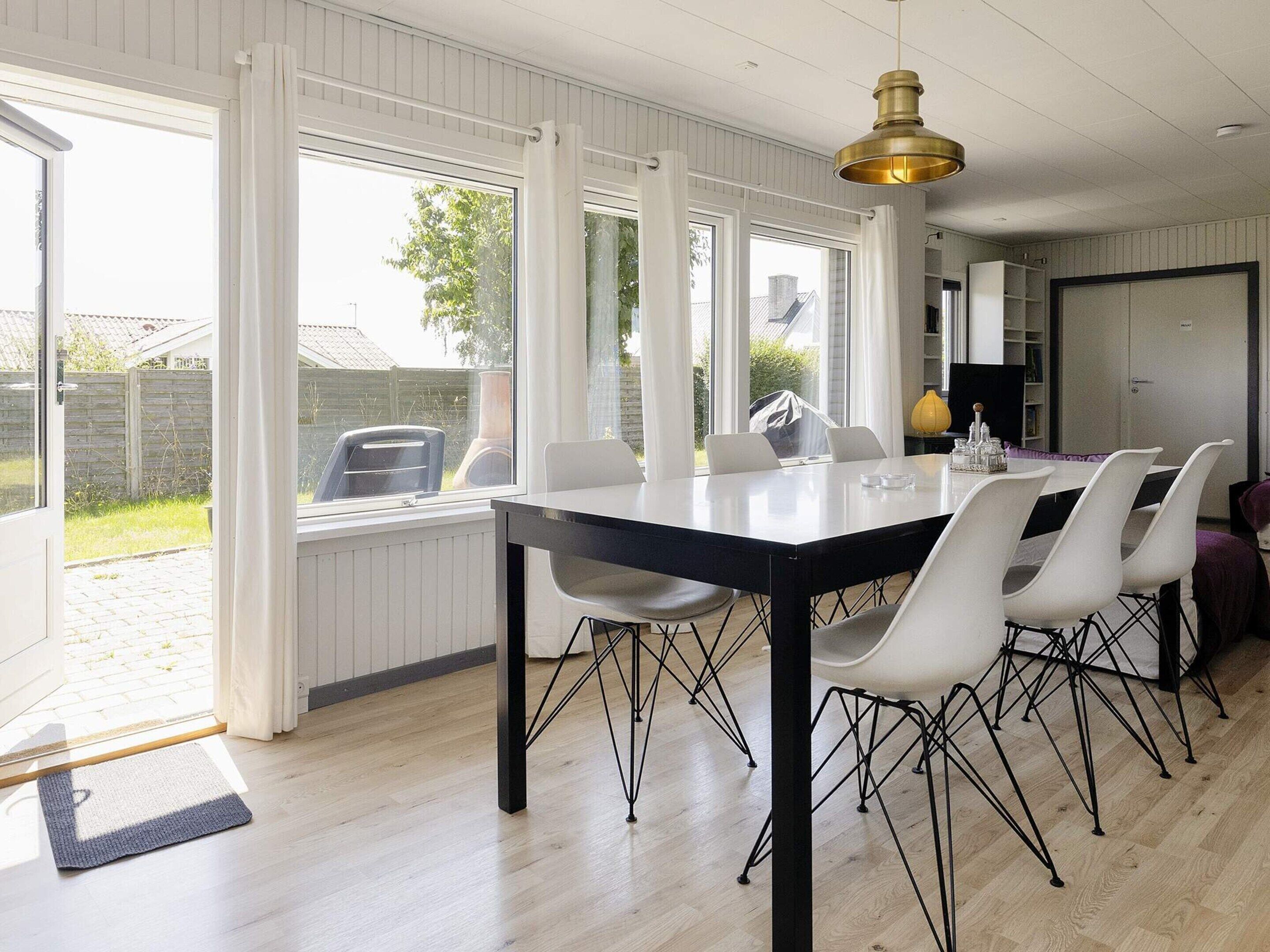 Een eetruimte met een tafel en stoelen, grote ramen en een hanglamp.