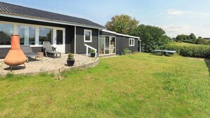 Ein modernes Haus mit Terrasse, Sitzgelegenheiten im Freien und einem großen Fenster.
