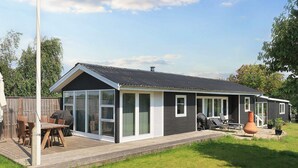 Ein einstöckiges Haus mit einer Terrasse, großen Fenstern und einem Grillbereich.