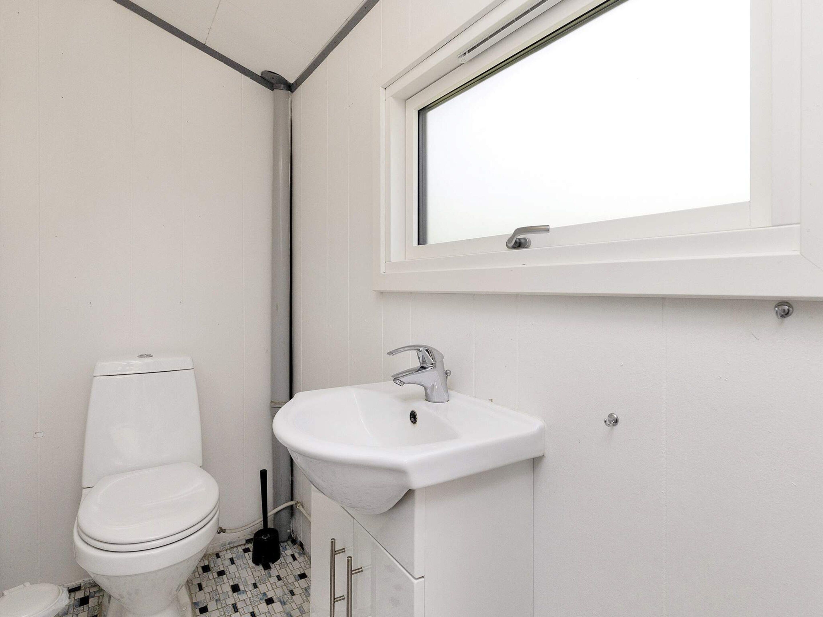 A bathroom with a toilet, sink, and window.