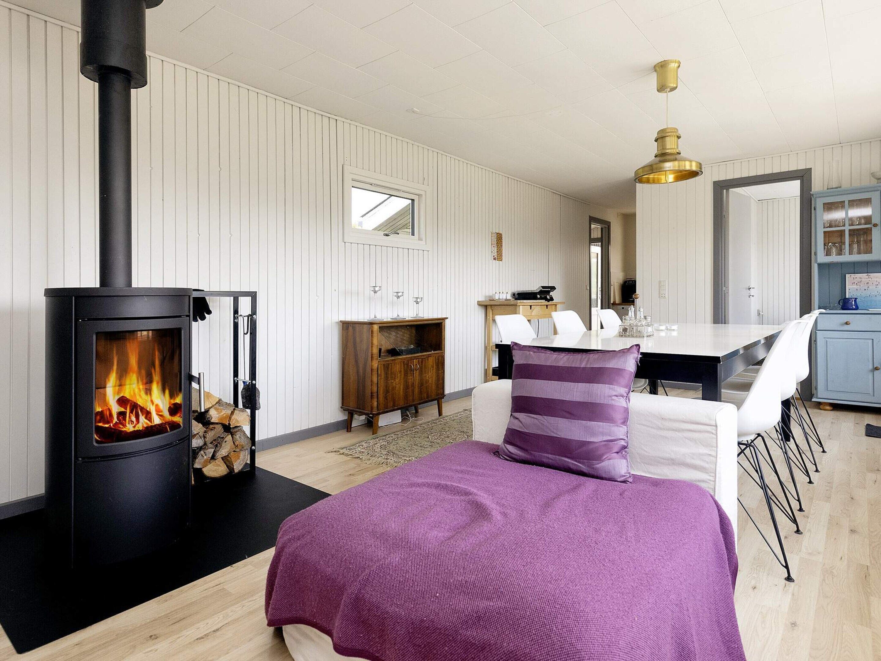 Una habitación acogedora con una estufa de leña, un comedor con mesa y sillas, y una cocina con armarios y un espejo.