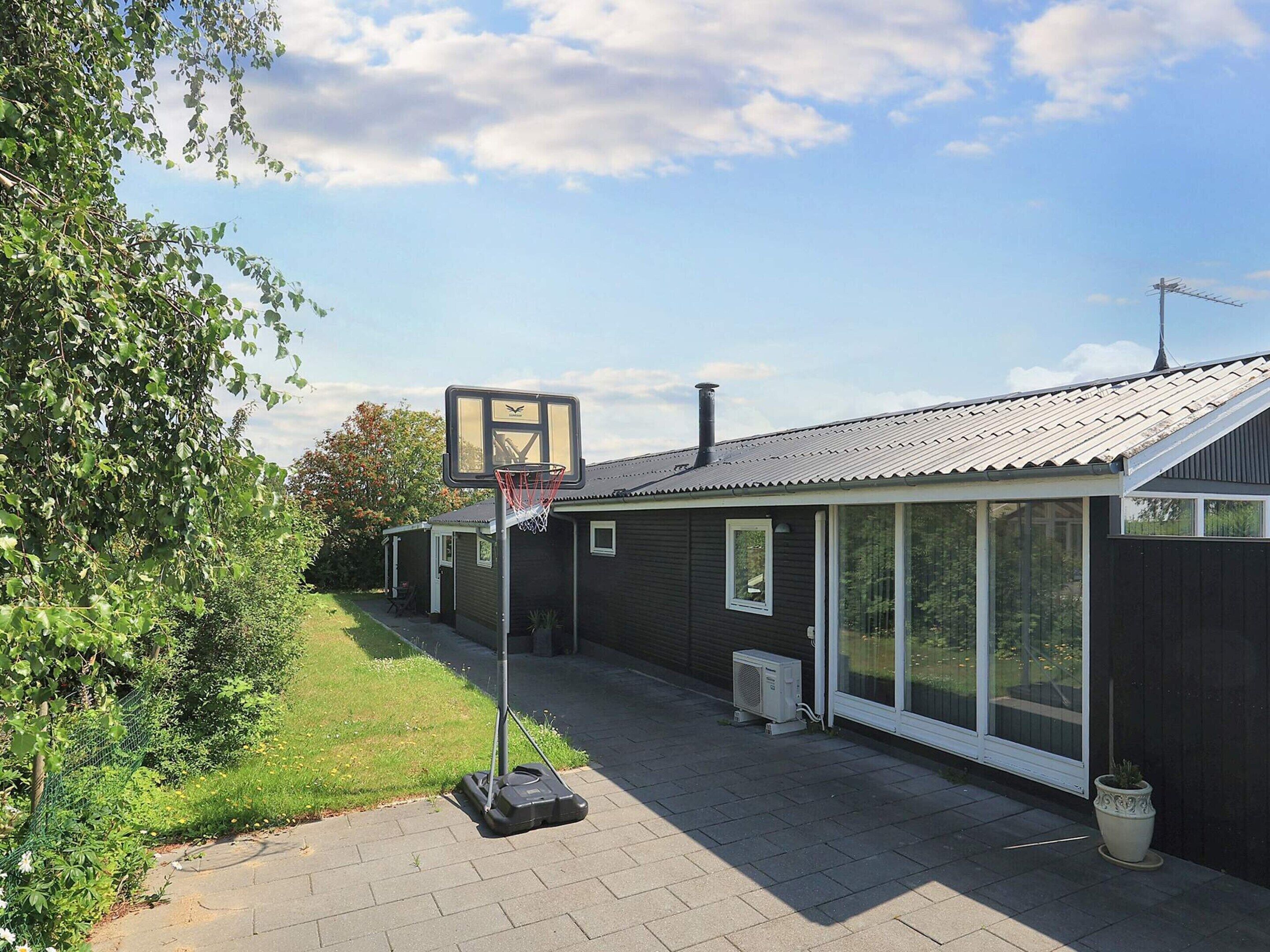 A residential building with a basketball hoop, a covered patio, and a large window.