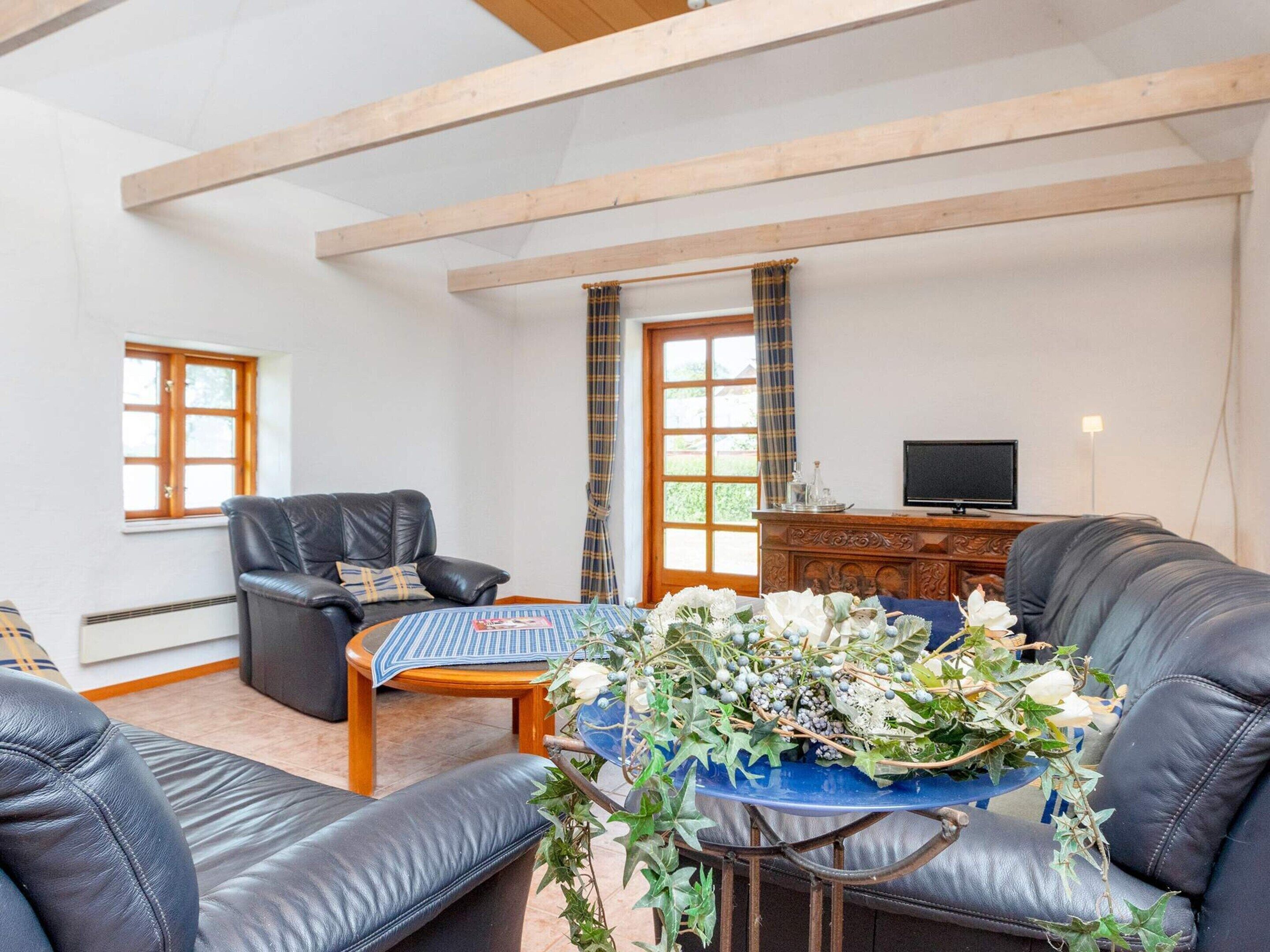 Una sala de estar con sofá, sillón, mesa de centro y televisor sobre un mueble de madera.