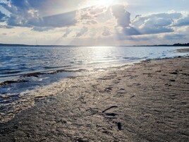A beach with a clear sky, calm sea, and a boat in the distance.