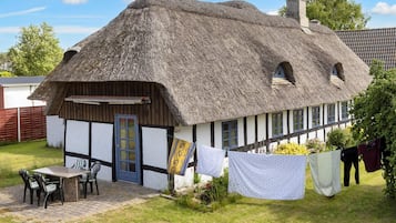 Una cabaña tradicional con techo de paja, un pequeño patio y mobiliario exterior.