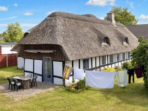 A traditional thatched-roof cottage with a small patio and outdoor seating. - 8 Person Holiday Home in Hadsund (Hadsund)