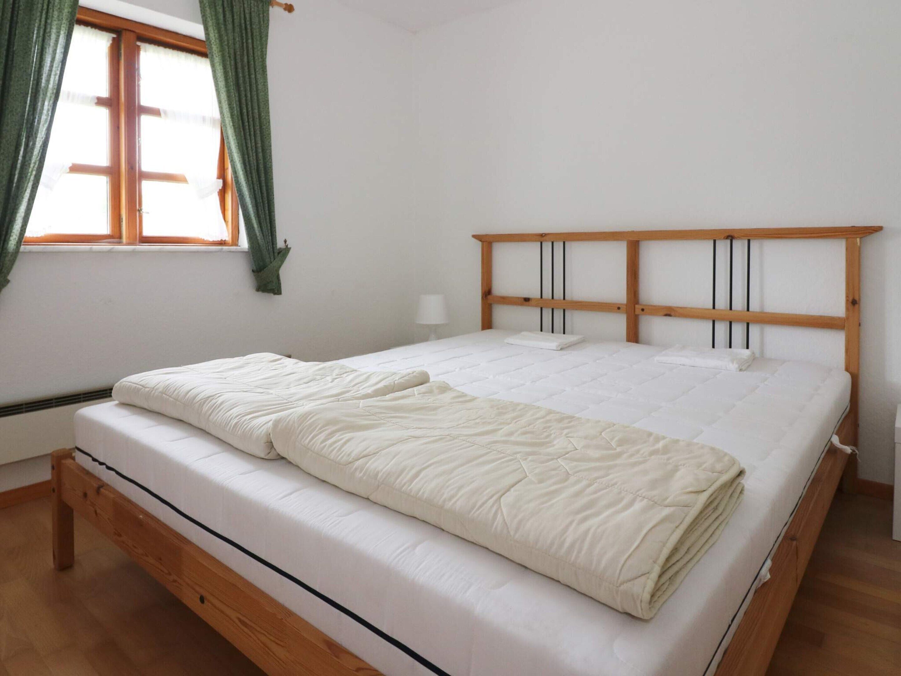 Habitación con una cama individual, cabecera de madera, ventana con cortinas y mesita de noche con lámpara.