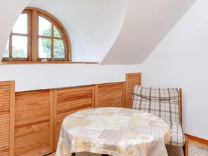 A room with a sloped ceiling, a wooden headboard, a plaid chair, and a table with a patterned tablecloth.