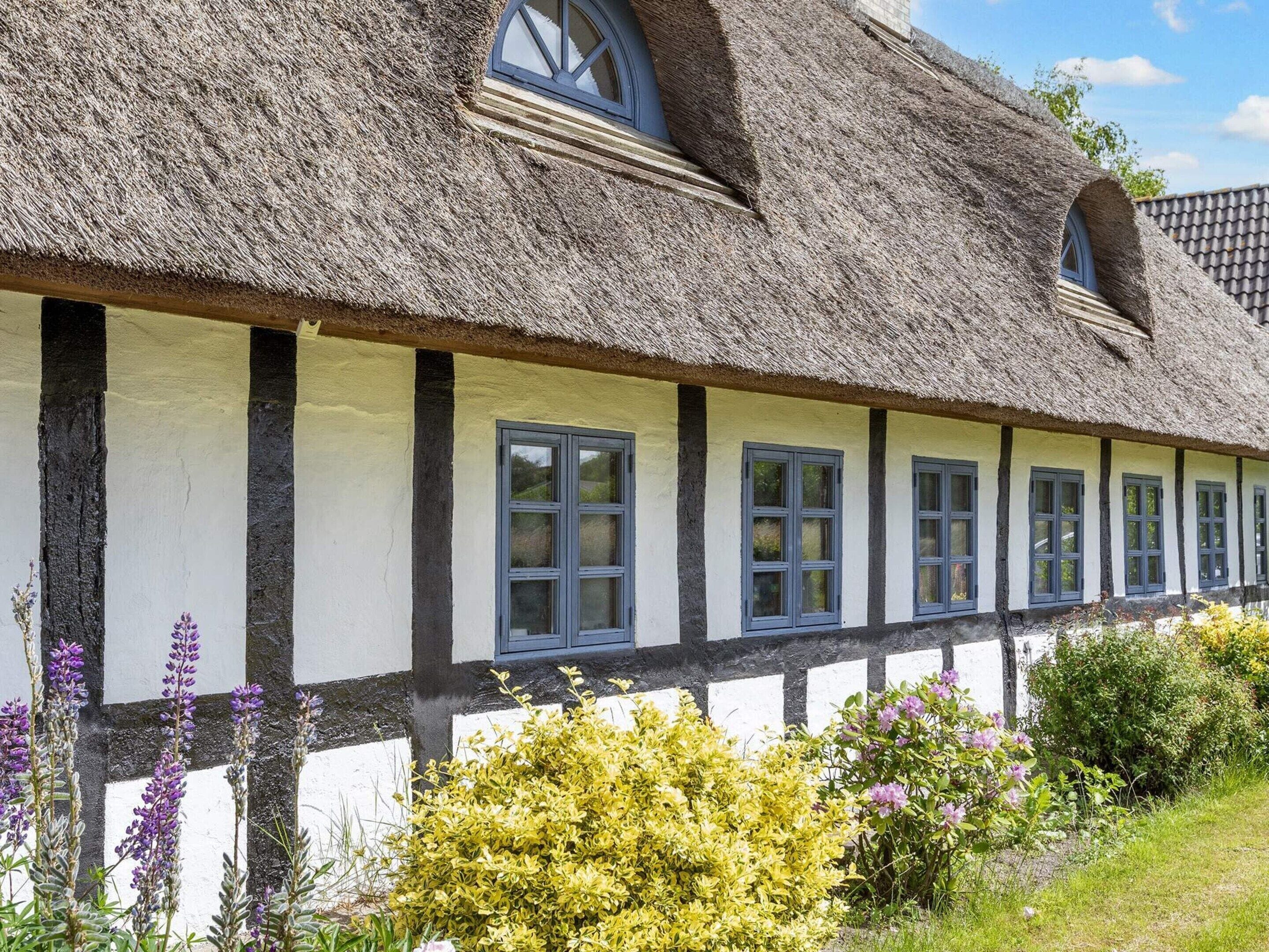 A traditional half-timbered house with a thatched roof and multiple windows.