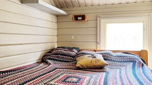 A room with a bed covered by a colorful knitted blanket, wooden walls, and a window with a view. - 8 Person Holiday Home in Ingaro (Ingaro)