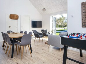 Un comedor moderno con una mesa y sillas de madera, mesa de fútbol de mesa y televisor en la pared.