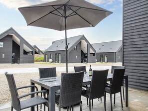 Un espace patio avec une table et des chaises, un grand parasol, et plusieurs bâtiments modernes en arrière-plan.