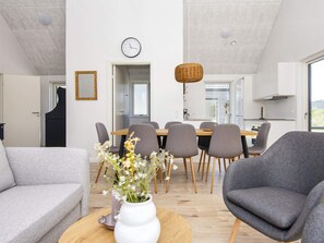 Un salon moderne avec un canapé, un fauteuil, une table à manger avec des chaises, un vase de fleurs et une horloge au mur.