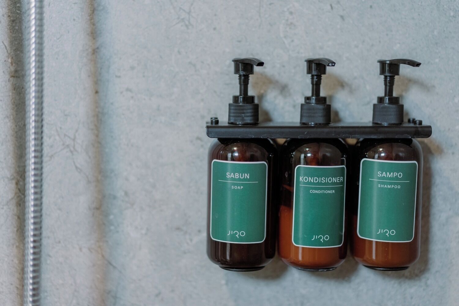 Three bottles of shampoo, conditioner, and soap on a rack against a wall.