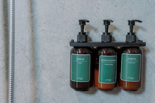 Three bottles of shampoo, conditioner, and soap on a rack against a wall. - Jiro Hotel (Bandung)