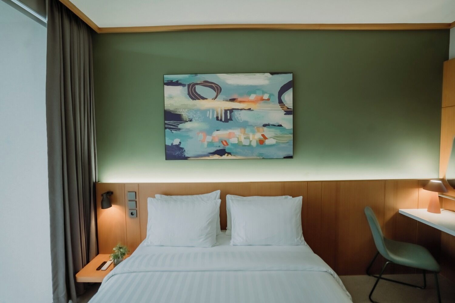 Een hotelkamer met een bed, een bureau en een schilderij aan de muur.