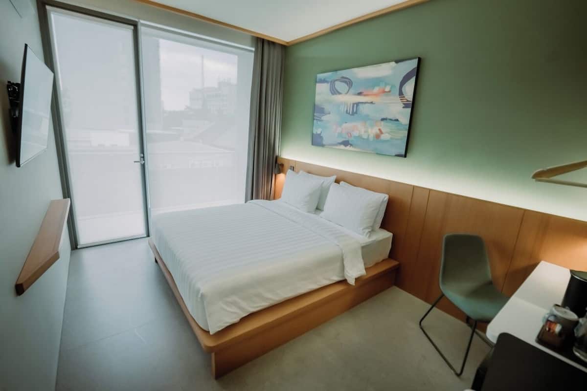 Quarto de hotel com cama, escrivaninha, cadeira, um quadro e vista para o exterior.