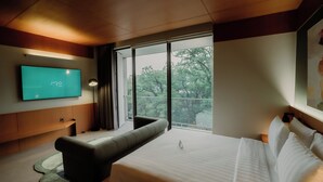 Une chambre d’hôtel moderne dotée d’un grand lit, d’un téléviseur à écran plat fixé au mur, d’un canapé et d’une grande fenêtre donnant sur la verdure.