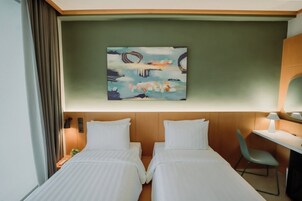 Habitación de hotel con dos camas, un escritorio, una silla, un cuadro en la pared y una ventana con cortinas.