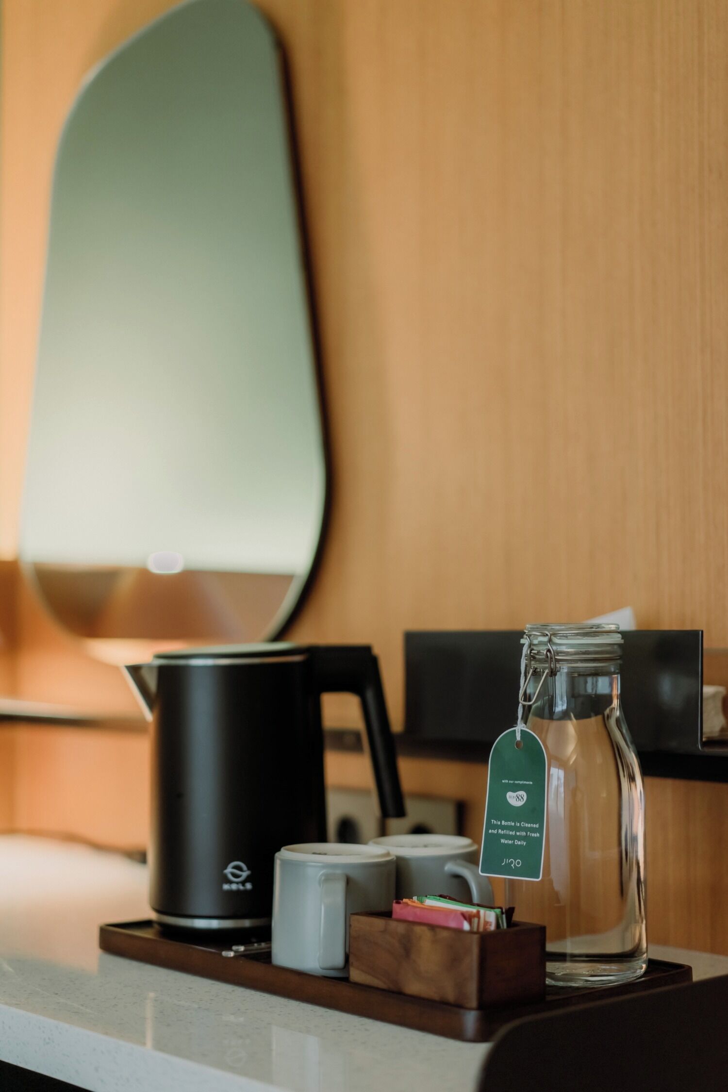 A coffee station with a coffee maker, a glass jar with a tag, and a mug on a wooden tray.