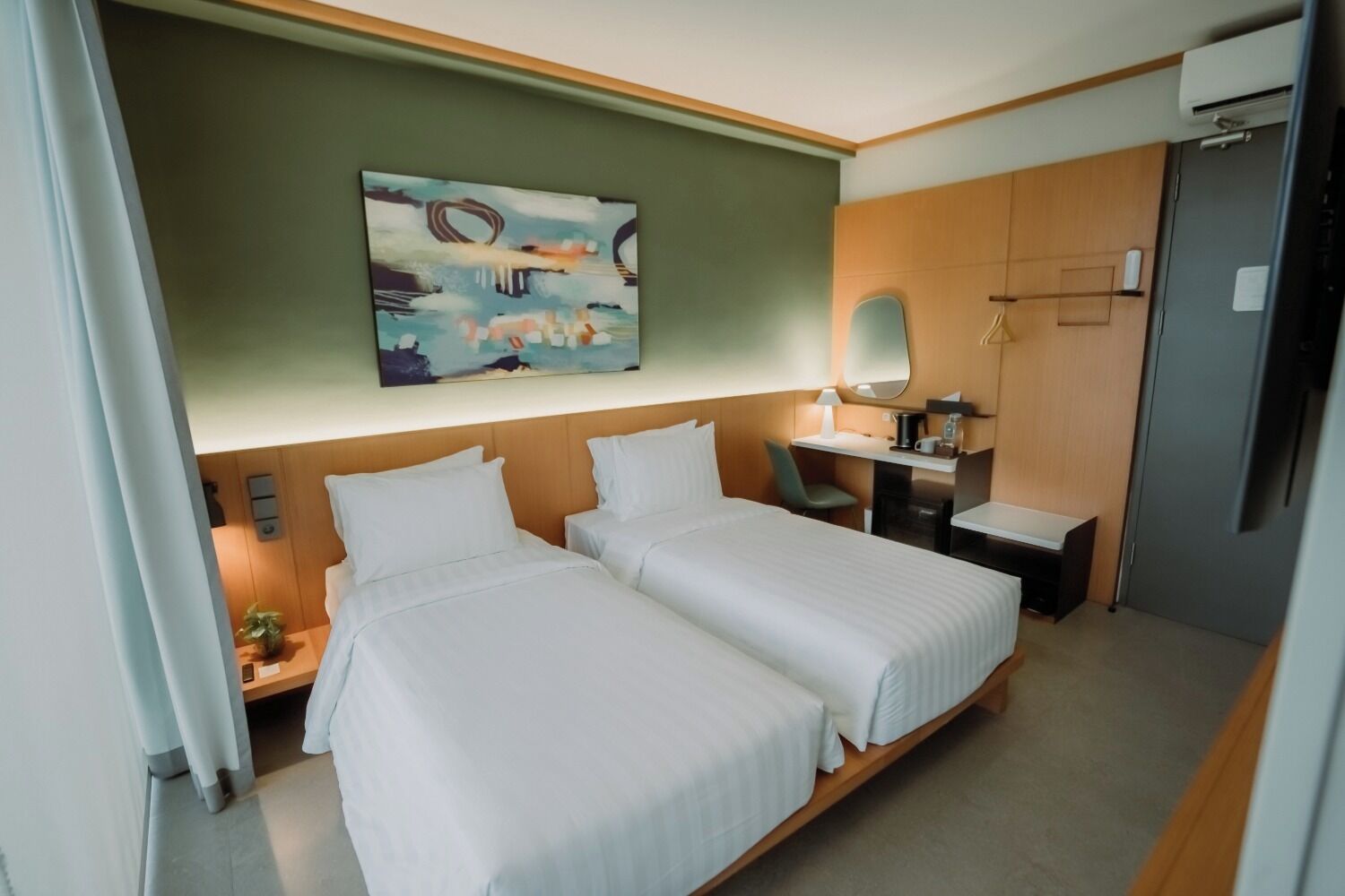 Ein Hotelzimmer mit zwei Betten, einem Schreibtisch, einem Stuhl, einem kleinen Tisch, einem Spiegel und einem Bild an der Wand.