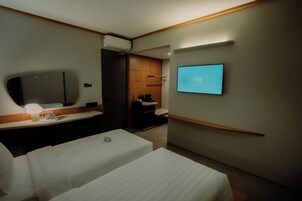 Quarto de hotel moderno com cama, mesa de cabeceira e TV fixada na parede.