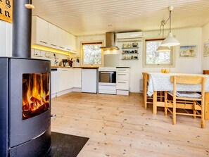 A modern kitchen with a wood-burning stove, white cabinetry, and a dining area with a table and chairs. - 8 Person Holiday Home in Pandrup (Pandrup)