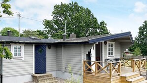 A small, single-story house with a blue door, a wooden deck, and a covered outdoor seating area. - 4 Star Holiday Home in Drottningskar (Drottningskär)