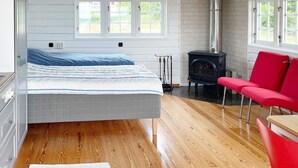 A room with a bed, a red chair, a wooden floor, and a fireplace. - 4 Star Holiday Home in Drottningskar (Drottningskär)