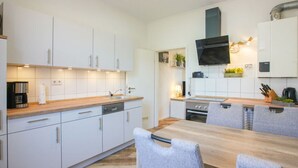 A modern kitchen with white cabinets, a wooden countertop, a built-in oven, and a dining area with a table and chairs. - At Home Comfortable Holiday Residence (Borkum)