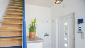 A staircase with wooden steps and a blue handrail, leading to a landing with a white door and a wall-mounted light fixture. - At Home Comfortable Holiday Residence (Borkum)