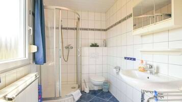 Un baño con ducha, inodoro y lavabo, con azulejos blancos y piso azul.
