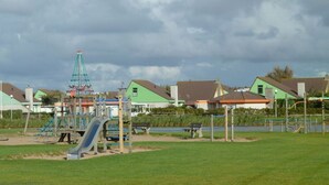 A playground with a slide and climbing structures, surrounded by houses and a body of water. - "sina" Comfortable Holiday Residence (Julianadorp)