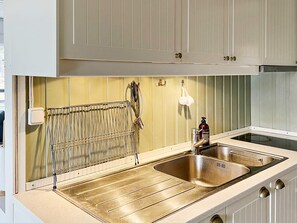A kitchen with a stainless steel sink, a built-in oven, and a hanging rack. - 4 Star Holiday Home in Vato (Vätö)