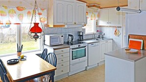 Une cuisine avec des meubles blancs, un four à micro-ondes, une cuisinière et un évier. On y trouve une table à manger avec des chaises et un luminaire suspendu.