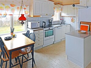 A kitchen with white cabinets, a microwave, a stove, and a sink. There is a dining table with chairs and a hanging light fixture. - 4 Star Holiday Home in Mellbystrand (Mellbystrand)