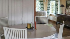 A round dining table with white chairs, a small decorative item on the table, and a window with curtains in the background. - 4 Star Holiday Home in Mellbystrand (Mellbystrand)