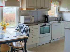 A kitchen with white cabinets, a microwave, an oven, a sink, and a dining table with chairs. - 4 Star Holiday Home in Mellbystrand (Mellbystrand)