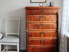 A wooden chest of drawers with multiple compartments, a white chair with a striped cushion, and a wall clock above the drawers. - 4 Star Holiday Home in Mellbystrand (Mellbystrand)