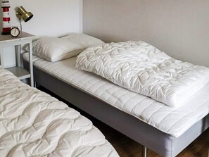 A single bed with a white quilted mattress and pillows, a bedside table with a lamp, and a wall-mounted clock. - 4 Star Holiday Home in Mellbystrand (Mellbystrand)