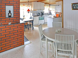 A kitchen with white cabinets, a microwave, and a sink. There is a dining table with chairs and a hanging light fixture. - 4 Star Holiday Home in Mellbystrand (Mellbystrand)