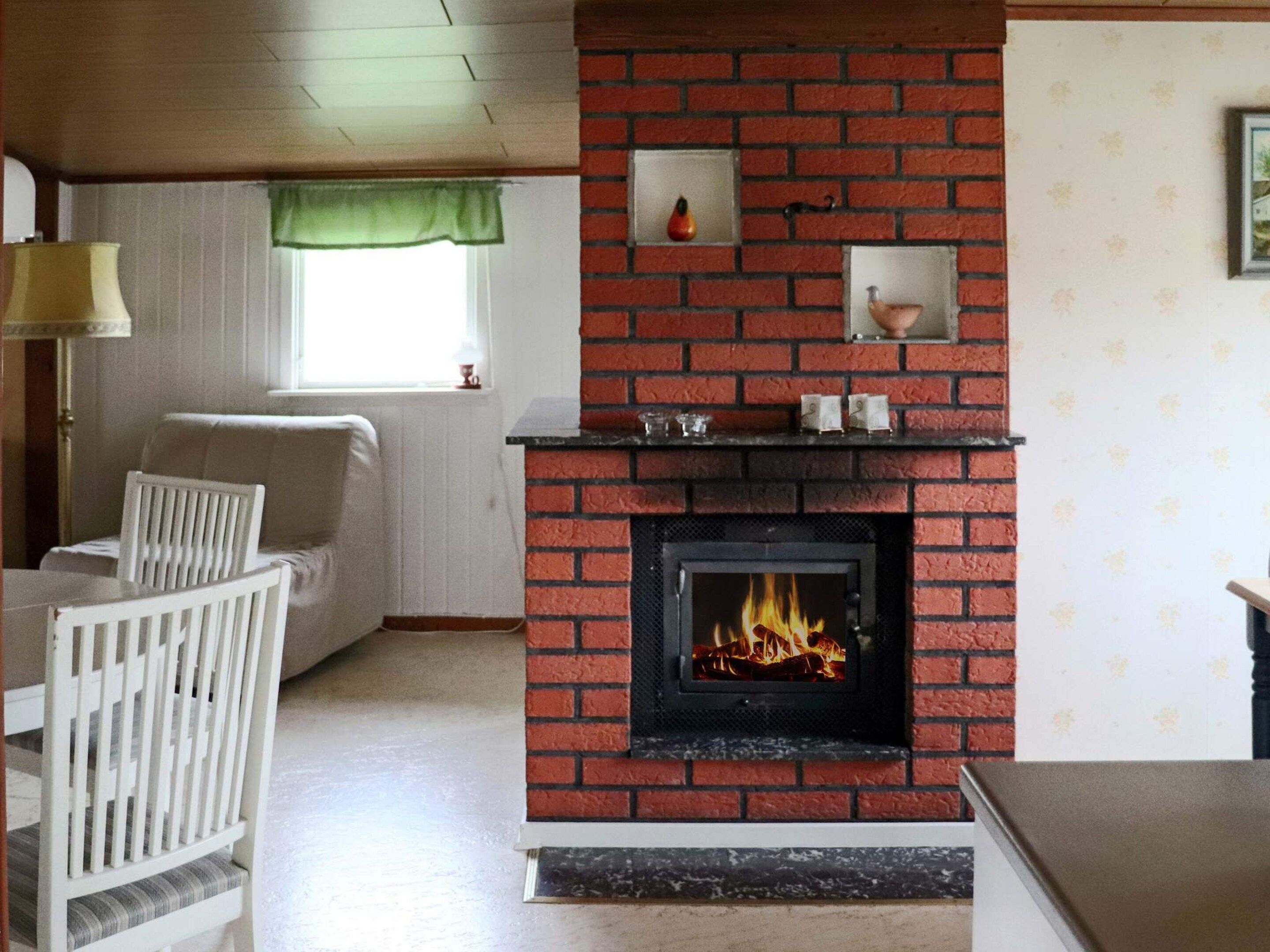 A living room with a brick fireplace, a sofa, a dining table with chairs, and a window with a green valance.