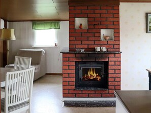 A living room with a brick fireplace, a sofa, a dining table with chairs, and a window with a green valance. - 4 Star Holiday Home in Mellbystrand (Mellbystrand)