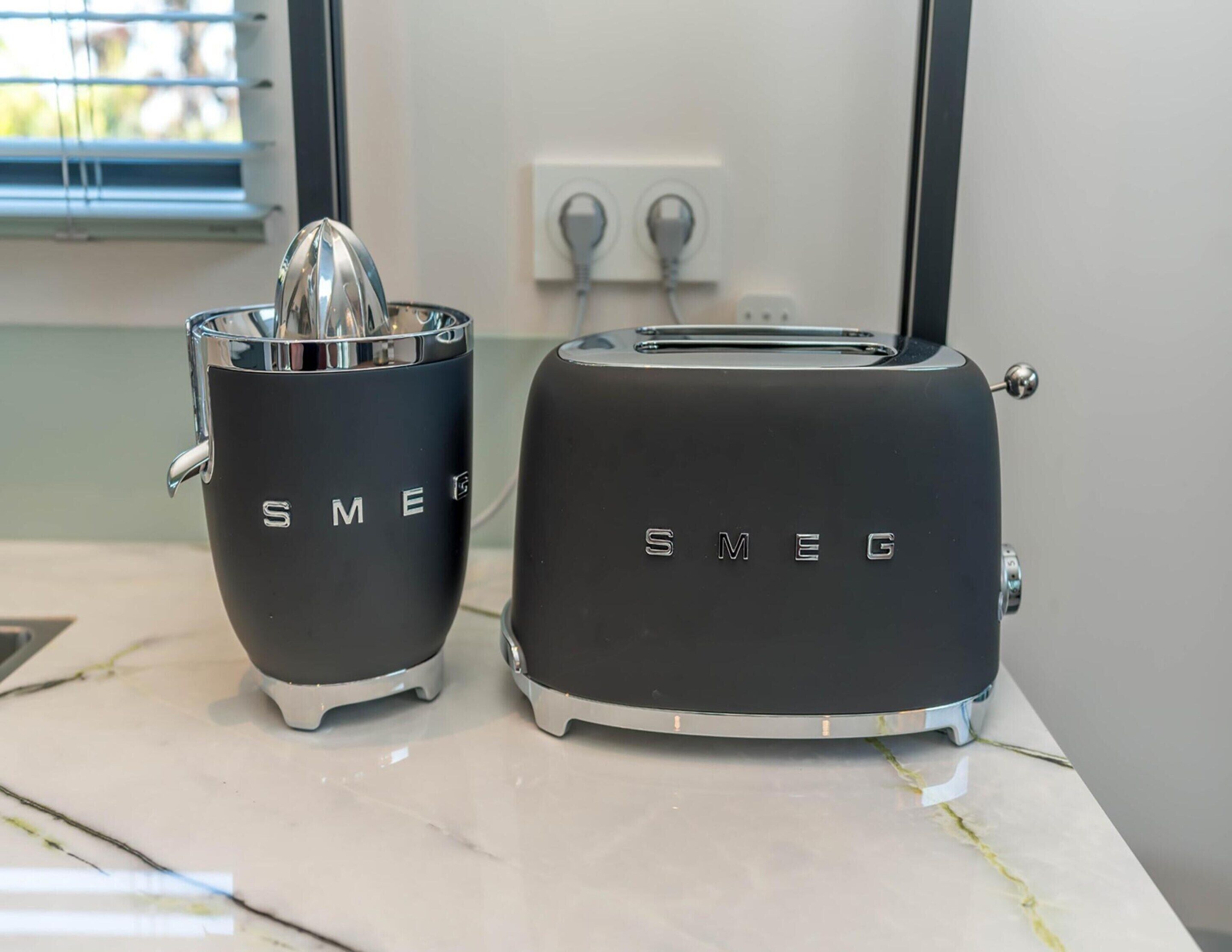 Twee keukenapparaten, een sapcentrifuge en een broodrooster, staan op een marmeren aanrecht.