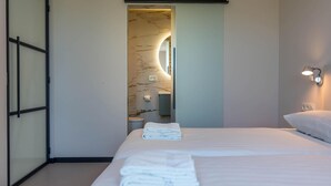 A modern hotel room with a large bed, a bathroom with a marble wall, and a mirror. - Energy-neutral Villa for 2 People (Oudeschild)