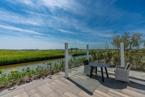 Eine Terrasse mit Glasgeländer, die auf einen Fluss blickt, mit Tisch und zwei Stühlen.