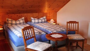 A cozy room with wooden ceiling and walls, featuring a bed with blue bedding and plaid pillows, two wooden chairs, and a small round table with a lace doily. - "haus Burck" Modern Retreat (Wankendorf)